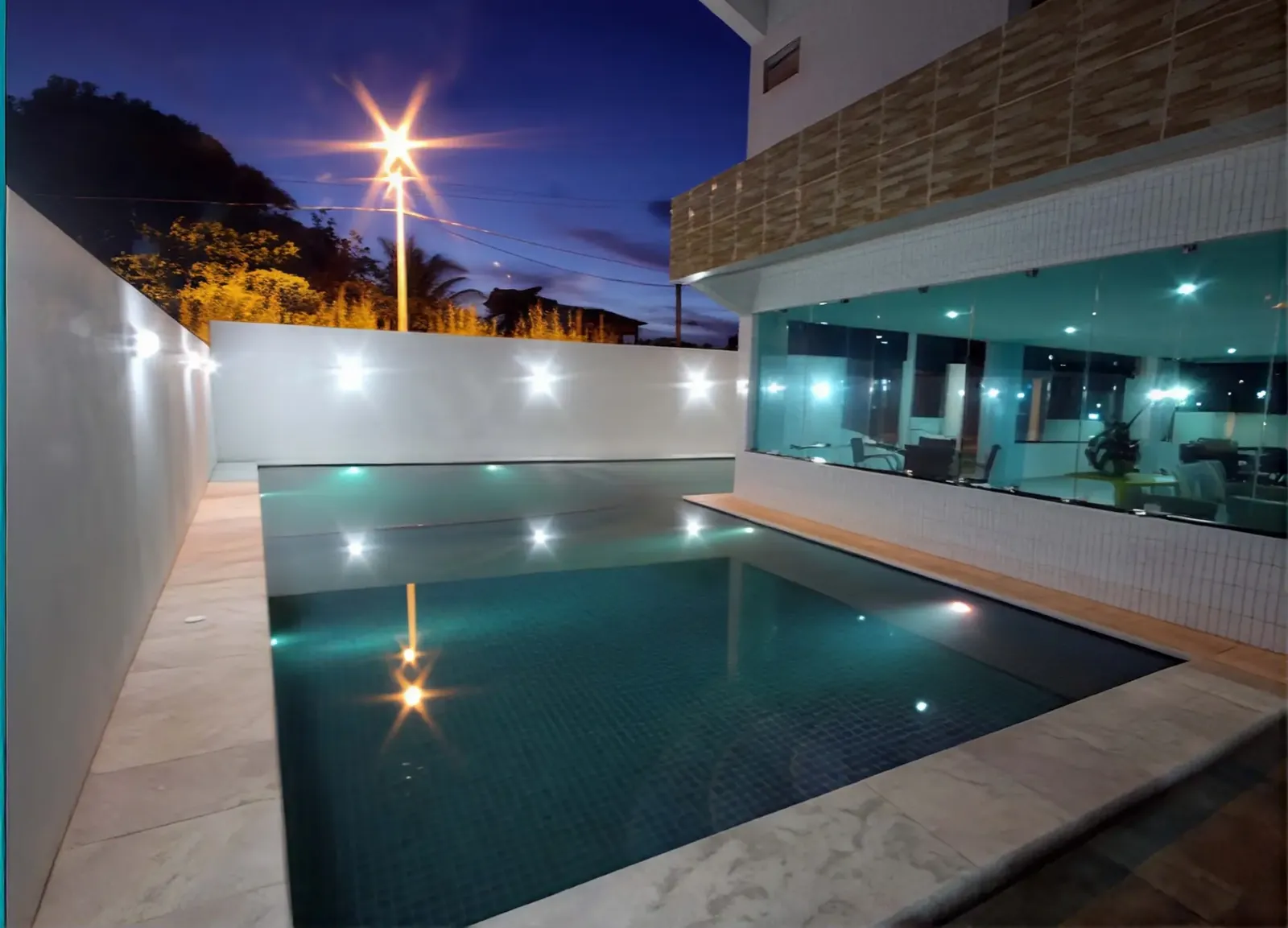Piscina ao ar livre ao entardecer, com luzes refletindo na água