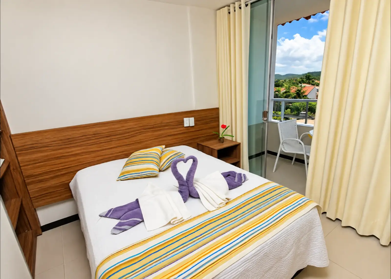 Quarto do apartamento com cabeceira de madeira e varanda com assentos externos